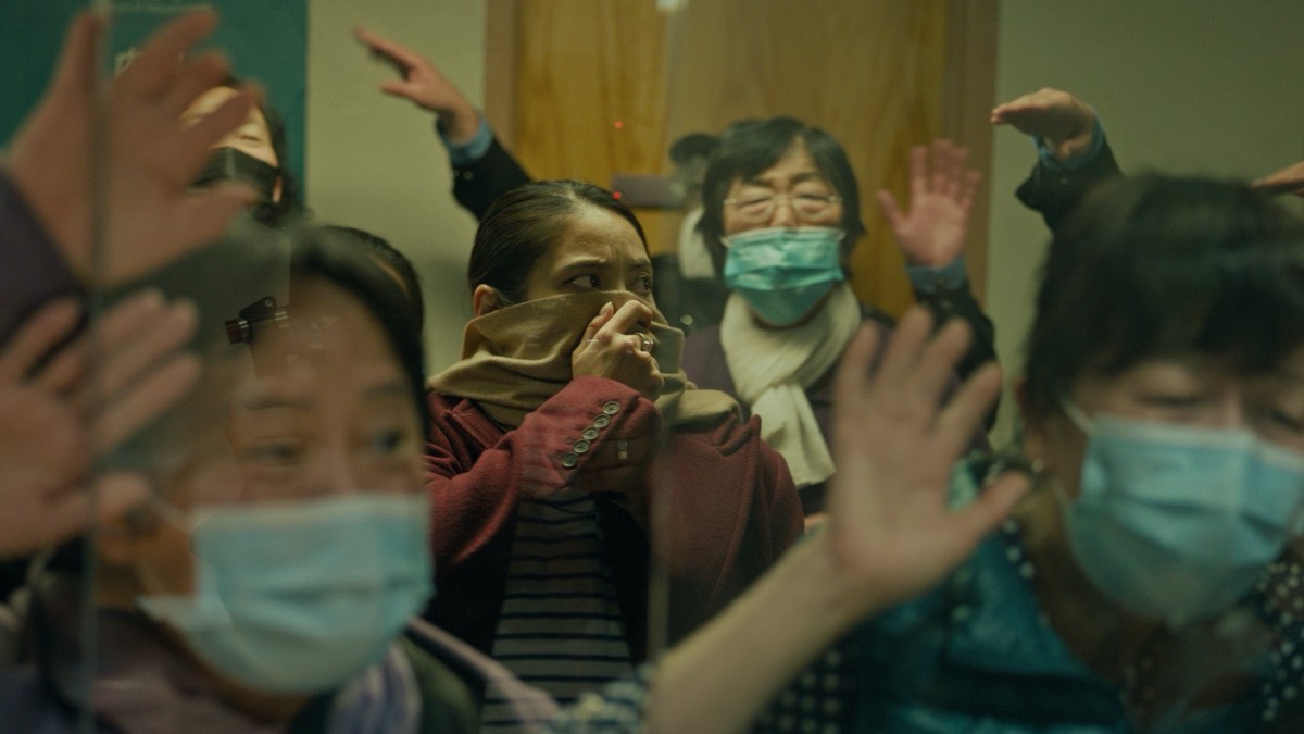《超限戰》劇照:醫院隔離區外戴口罩的民眾隔著玻璃伸手拍打,前景一名女子以圍巾掩住口鼻